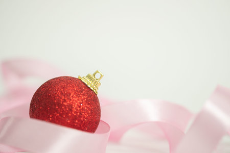 Red Christmas bauble with pink ribbon bow on white background.の写真素材