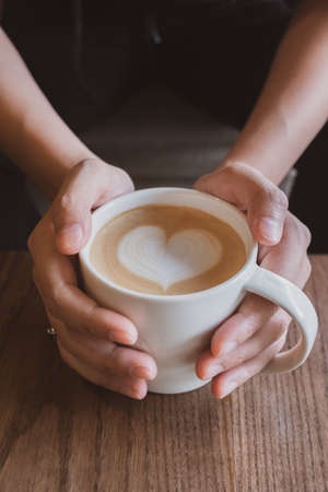 Hand holding a cup of coffee with heart foam milk.の写真素材