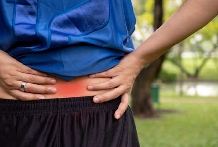 A young woman holding his back in pain in the garden.の写真素材