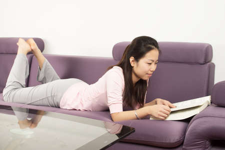 Young Oriental woman with book on sofaの写真素材