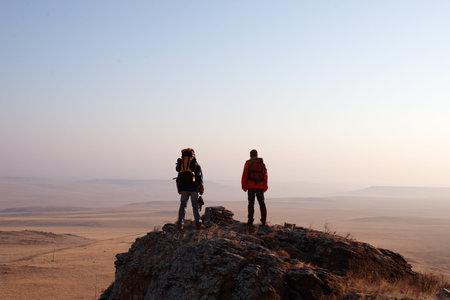 Two hikers enjoying sunrise from top of a mountain