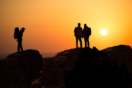 Three hiker with backpack top of a mountain and enjoying valley view during sunrise