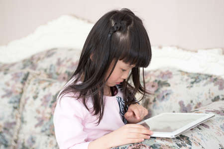 Little girl playing on the couch tablet Indoorsの写真素材