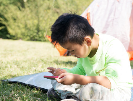 Boy playing with smartphone sitting on park lawnの写真素材