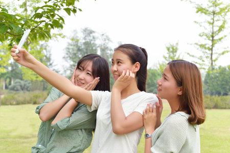 Three female students taking photo using mobile phoneの写真素材