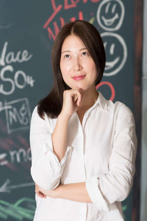 Thoughtful teenage girl with hand on chin against on blackboardの写真素材