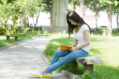 girl student holds a book to read. On the park bench.の写真素材