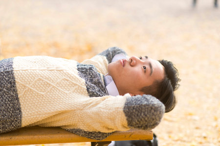 Male students lying on a bench in the outdoor look up at the skyの写真素材
