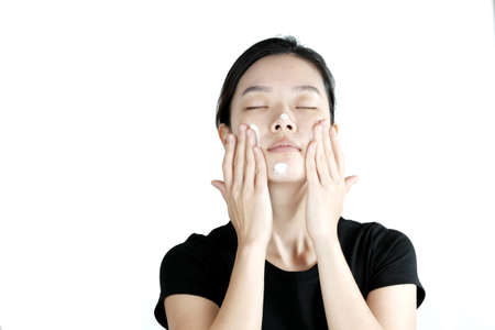 Asian girl applying cream lotion on face, isolated on white backgroundの写真素材