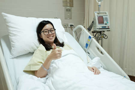 Asian patient girl thumbs up and smile while lying on hospital bedの写真素材