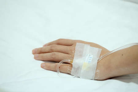 Patient hand injected with saline IV drip on hospital bedの写真素材