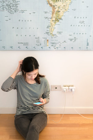 Cute asian girl frustrating with phone's battery, charging on the wall