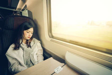 Beautiful asian girl sleeping on the train while listening to music, with copy space, soft warm light toneの写真素材