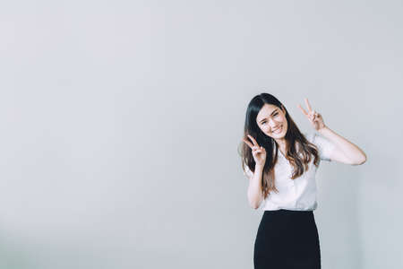 Cute asian university girl doing funny rabbit pose, copy space on gray wall backgroundの写真素材