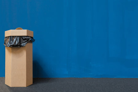 Waste bin or trash bin made of recycled paper, blue painted wall background with copy space, recycle...
