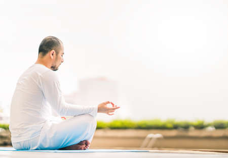Young man meditating by swimming pool, yoga or relax concept, city view background with copy spaceの写真素材