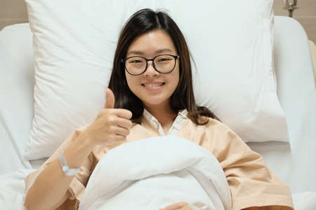 Beautiful Asian patient girl thumbs up and smile on hospital admission bed, medical or health concept