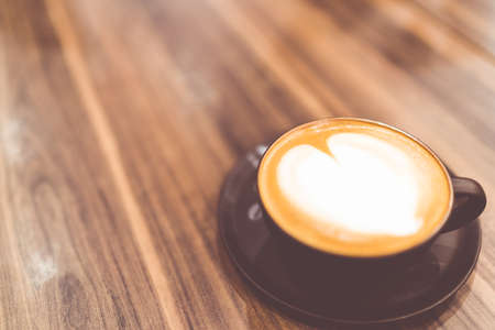 Cup of hot cappuccino coffee with heart shaped latte art whipped cream in vintage tone, copy space on wooden table, love or relax conceptの写真素材