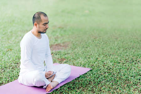 Handsome Asian man meditating on green grass in the park, calm and focused, health and yoga meditation concept, with copy spaceの写真素材