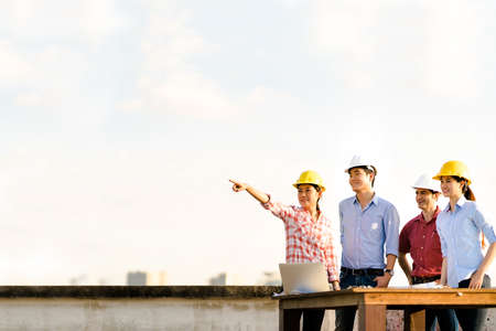 Multiethnic diverse group of engineers or business partners at construction site, pointing toward copy space on sky during sunset, engineering industry or architectural teamwork conceptの写真素材