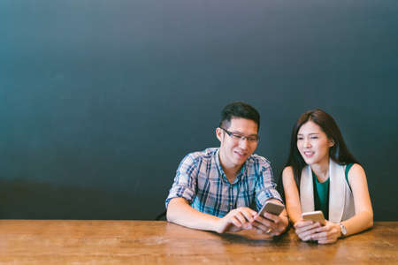 Young Asian couple or coworker using smartphone at cafe, modern lifestyle with gadget technology or casual business concept, with copy space