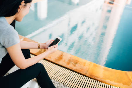 Woman hand holding smartphone by swimming pool, communication technology and relaxing modern lifestyle concept, with copy spaceの写真素材