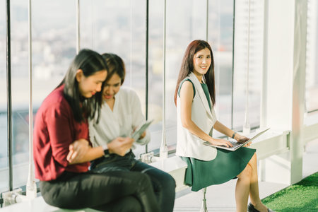 Beautiful Asian girls using laptop notebook and digital tablet during office break at sunset, modern lifestyle with gadget technology or working woman on casual business conceptの写真素材
