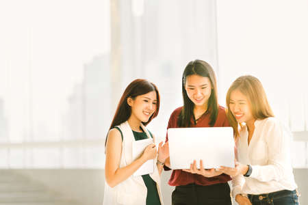 Three beautiful Asian girls on casual business meeting with laptop notebook and digital tablet at sunset, modern lifestyle with gadget technology or working women concept, with copy spaceの写真素材