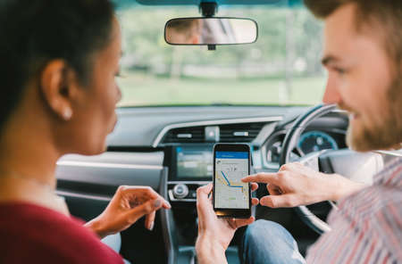 Multiethnic lover couple using navigation system on smartphone in car. Mobile phone application or modern gadget technology or family travel conceptの写真素材