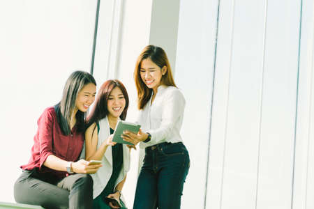 Three beautiful Asian girls using digital tablet together. Working woman or college students chatting at office with copy space. Modern lifestyle with gadget technology or casual business conceptの写真素材