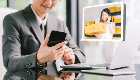 Businessman CEO order product box from young female Asian small business owner using phone, laptop. Online marketing shipping delivery service, e-commerce technology, or telemarketing startup SMEの写真素材