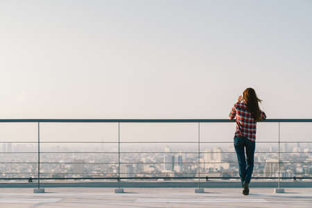 Woman using mobile phone at rooftop during sunset with copy space, communication or lonely people conceptの写真素材