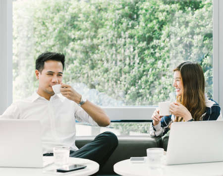 Young Asian couple or coworkers having coffee break while working on laptop computer at cafe or coffee shop. Leisure, casual work, love, or friendship concept. With copy spaceの写真素材