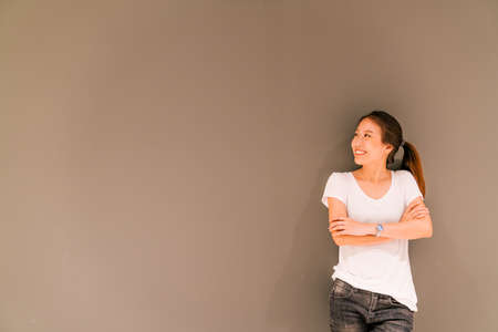 Beautiful Asian girl standing on grey wall background, looking at copy spaceの写真素材
