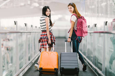 Two happy Asian girls traveling abroad together, carrying suitcase luggage in airport. Air travel or holiday vacation concept