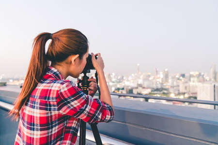 Long hair Asian woman taking cityscape photo on building rooftop in low light situation. Photography or hobby concept. With copy spaceの写真素材