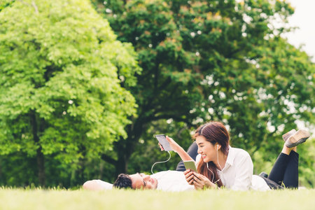 Young Asian lovely couple or college students listening to music together in the garden, with copy space. Leisure activity, Love relationship, wedding, or relaxing casual lifestyle conceptの写真素材