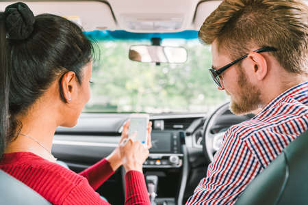 Multiethnic lover couple, white man and black Asian girl using navigator system app on smart phone in car. Modern gadget lifestyle, family travel activity, or online taxi call request service concept.の写真素材
