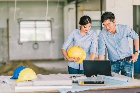 Young Asian engineers couple work together using notebook computer at building construction site....