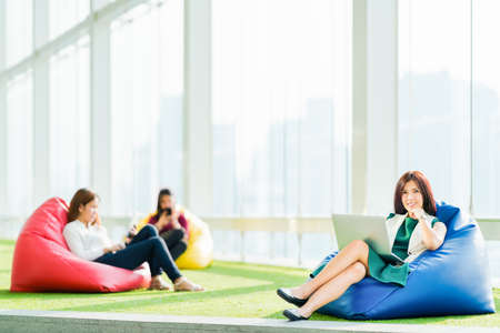 Asian students or business team sit together using laptop, digital tablet, smartphone in urban public space park. Modern casual office, Social media, wireless gadget, online shopping lifestyle conceptの写真素材