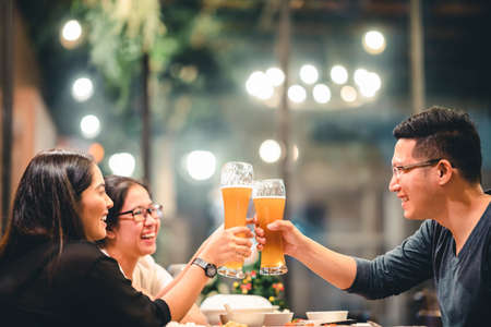 Group of Asian friends or coworkers cheering with beer, celebrating together at restaurant or night club. Young people toasting at party event after work. Success or friendship concept. Focus on glassの写真素材