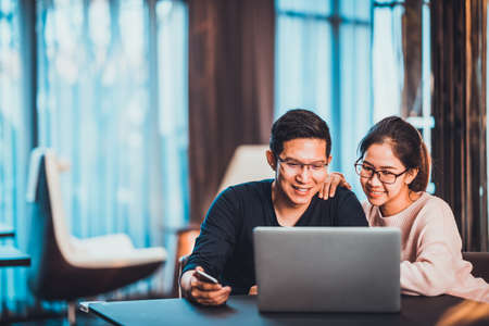 Young Asian married couple working together using laptop at home or modern office with copy space. Startup family business, SME entrepreneur, business partner, love relationship, or freelance conceptの写真素材