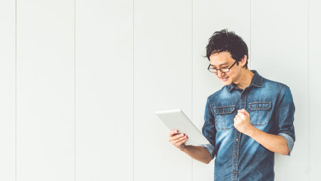 Young handsome happy Asian man celebrate success pose, using digital tablet, with copy space. Successful people, startup business, or college student education conceptの写真素材
