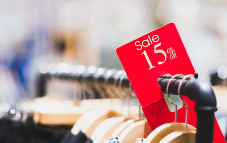 Red sale sign 15% discount on clothing rack in modern shopping mall or department store with copy space. Retail shop promotional event, new product discount, or business marketing advertising conceptの写真素材