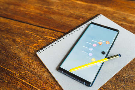 Bangkok, Thailand - Aug 30, 2018: Ocean Blue Samsung Galaxy Note 9 with yellow S pen stylus on a notebook, copy space on wooden table. Screen displaying note and drawing apps. Illustrative Editorial.のeditorial素材