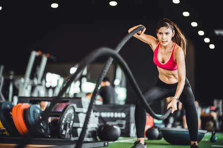 Beautiful Asian woman exercise on battling ropes training equipment in indoor fitness gym. Sport recreational activity, people workout, or healthy lifestyle conceptの写真素材