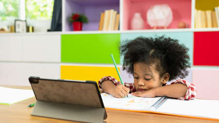 Young African American kid girl studying using digital tablet, preschool child study at home school. Children education, self isolation, coronavirus outbreak social distancing or homeschooling conceptの写真素材