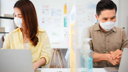 Asian business people wear face mask, wash hand using hand sanitizer, and separated by partition stand. Social distancing at work, new normal office lifestyle after coronavirus lockdown conceptの写真素材