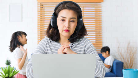 Young Asian mother work at home with kids playing and dancing in living room. New normal lifestyle, remote video call online conference meeting conceptの写真素材