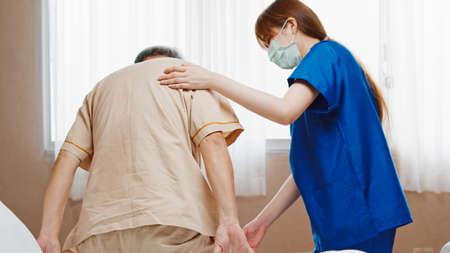 Female Asian nurse support senior male patient stand up and walk from bed in hospital. Nursing home, medical service, physiotherapy, hospitality, or recovery treatment conceptの素材 [FY310156502131]